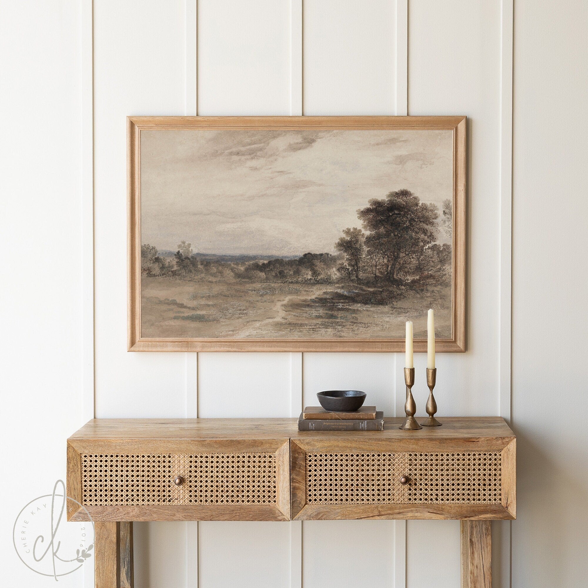 Framed vintage landscape art print featuring a rustic country scene with trees and a winding path, displayed above a wooden console table with a neutral-toned decor setting, perfect for farmhouse or modern rustic home decor.