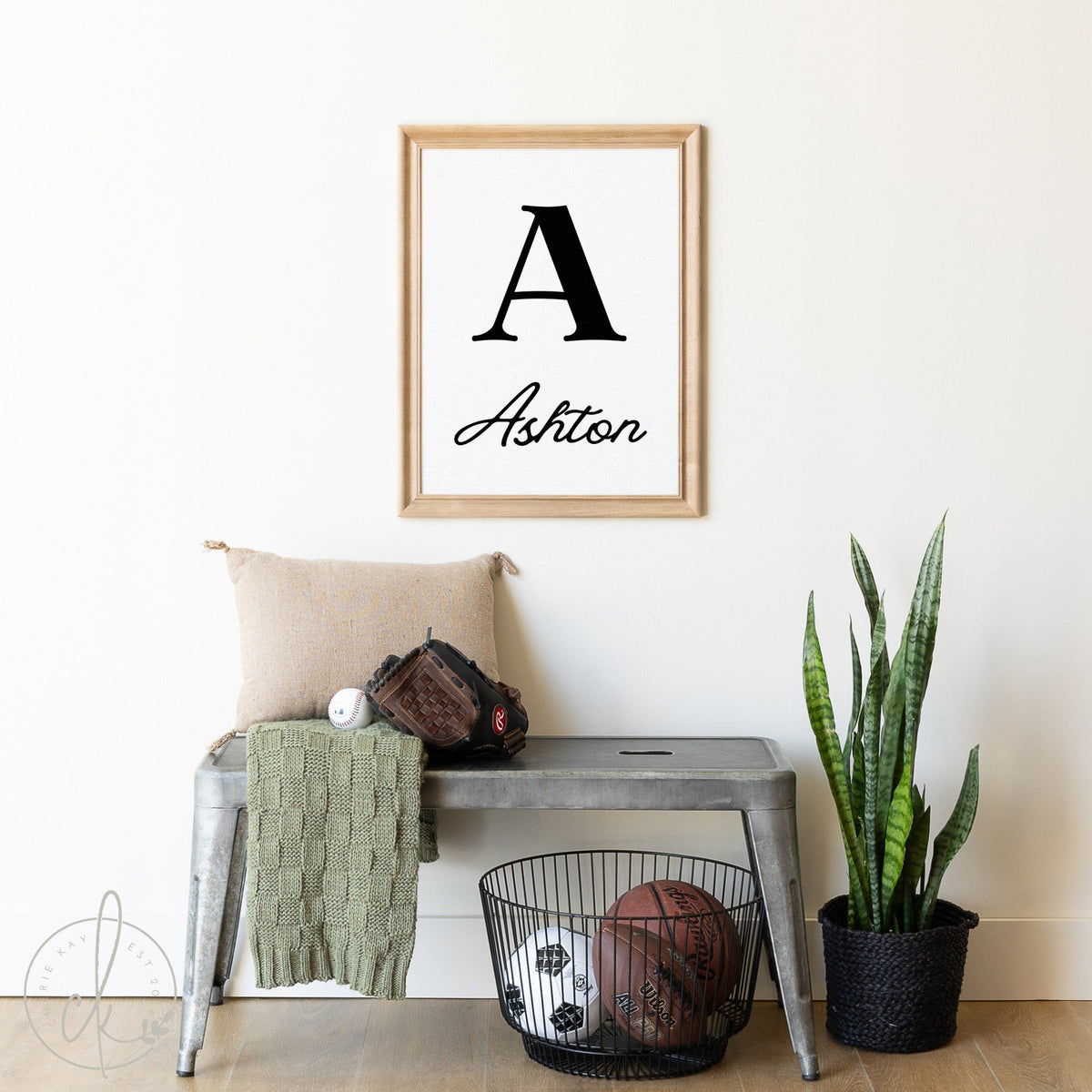 Personalized name sign for a nursery or kids room featuring a bold initial &amp;#39;A&amp;#39; and the name &amp;#39;Ashton&amp;#39; in elegant script, framed and displayed above a bench with sports equipment and a green plant nearby.