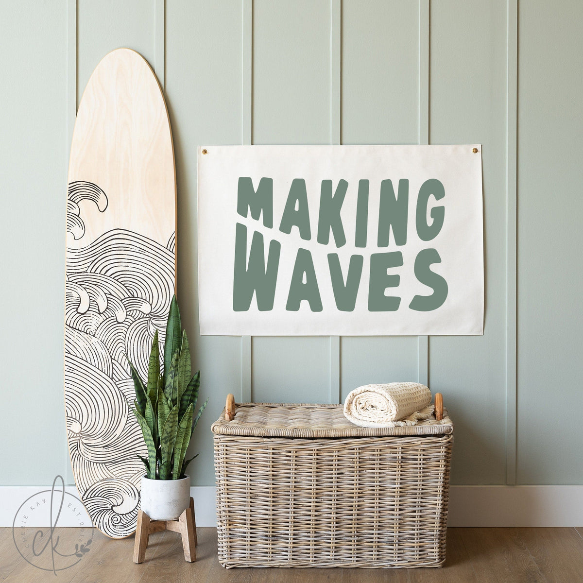 A decorative wall flag with the words Making Waves in green lettering, is displayed next to a surfboard with wave patterns and a wicker basket, adding a coastal touch to the room.