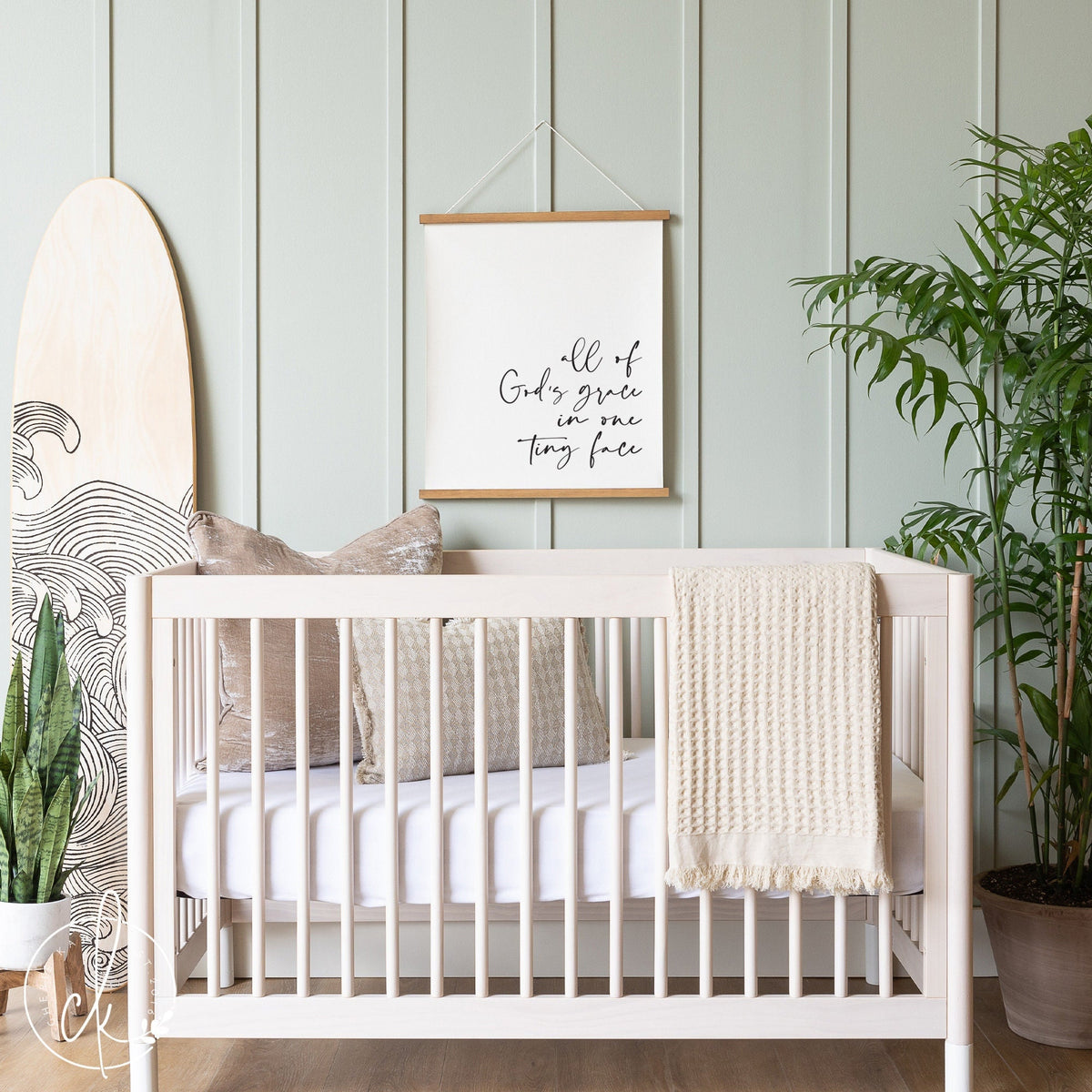 Neutral nursery with light wood crib, cozy pillows, and a canvas sign that reads All of God&amp;#39;s grace in one tiny face, creating a serene and faith-inspired baby room decor.