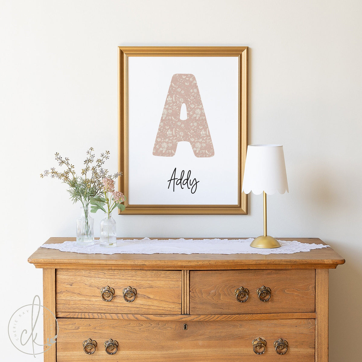 A beautifully decorated wooden dresser with a framed personalized floral monogram wall art above it. The monogram features the letter &amp;quot;A&amp;quot; with a floral pattern and the name &amp;quot;Addy&amp;quot; written underneath in elegant script.