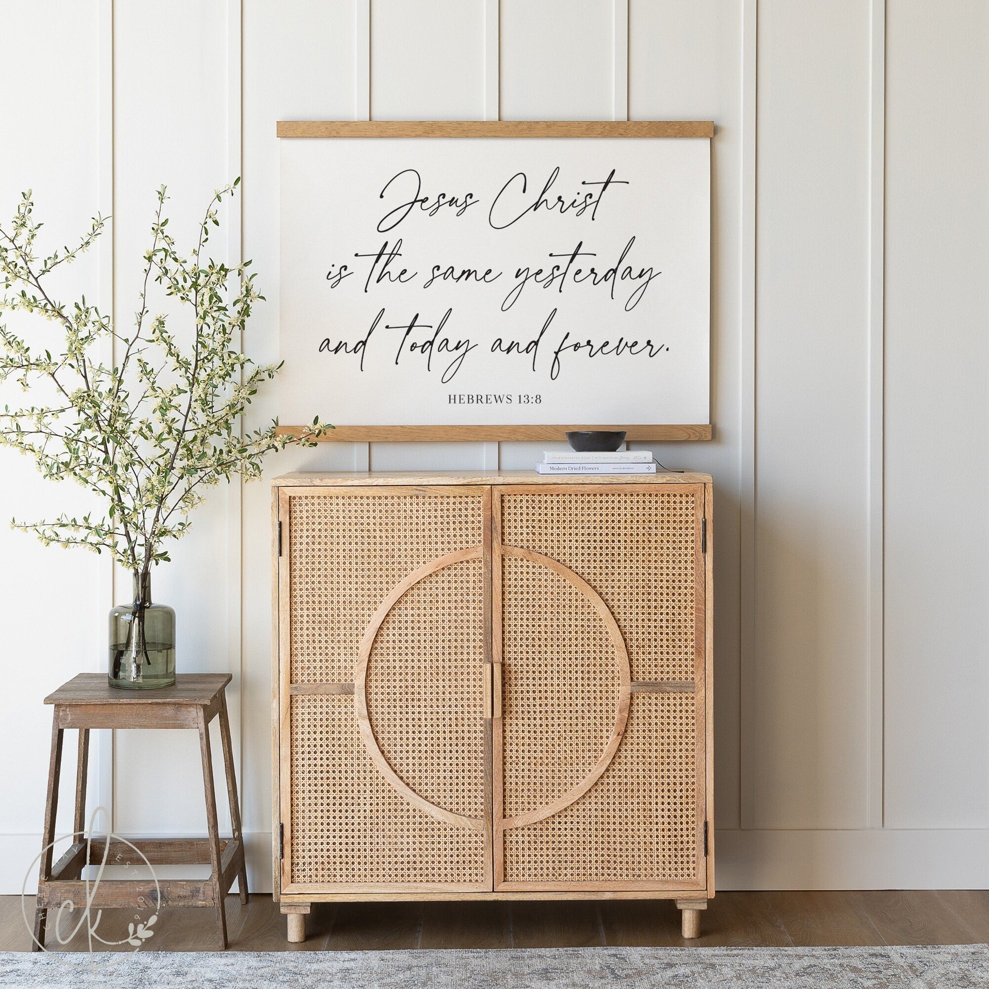 Christian wall decor featuring Hebrews 13:8 Bible verse on a canvas tapestry, displayed in a serene home setting with a wooden console table, a potted plant, and a cozy, neutral-toned interior design.