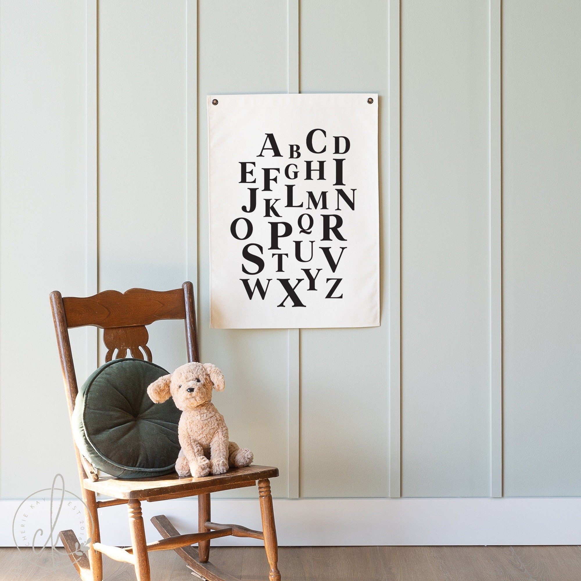 A cozy children&#39;s room featuring a canvas flag with an alphabet design hanging on a light green paneled wall. Creating a warm and inviting atmosphere ideal for learning and play.