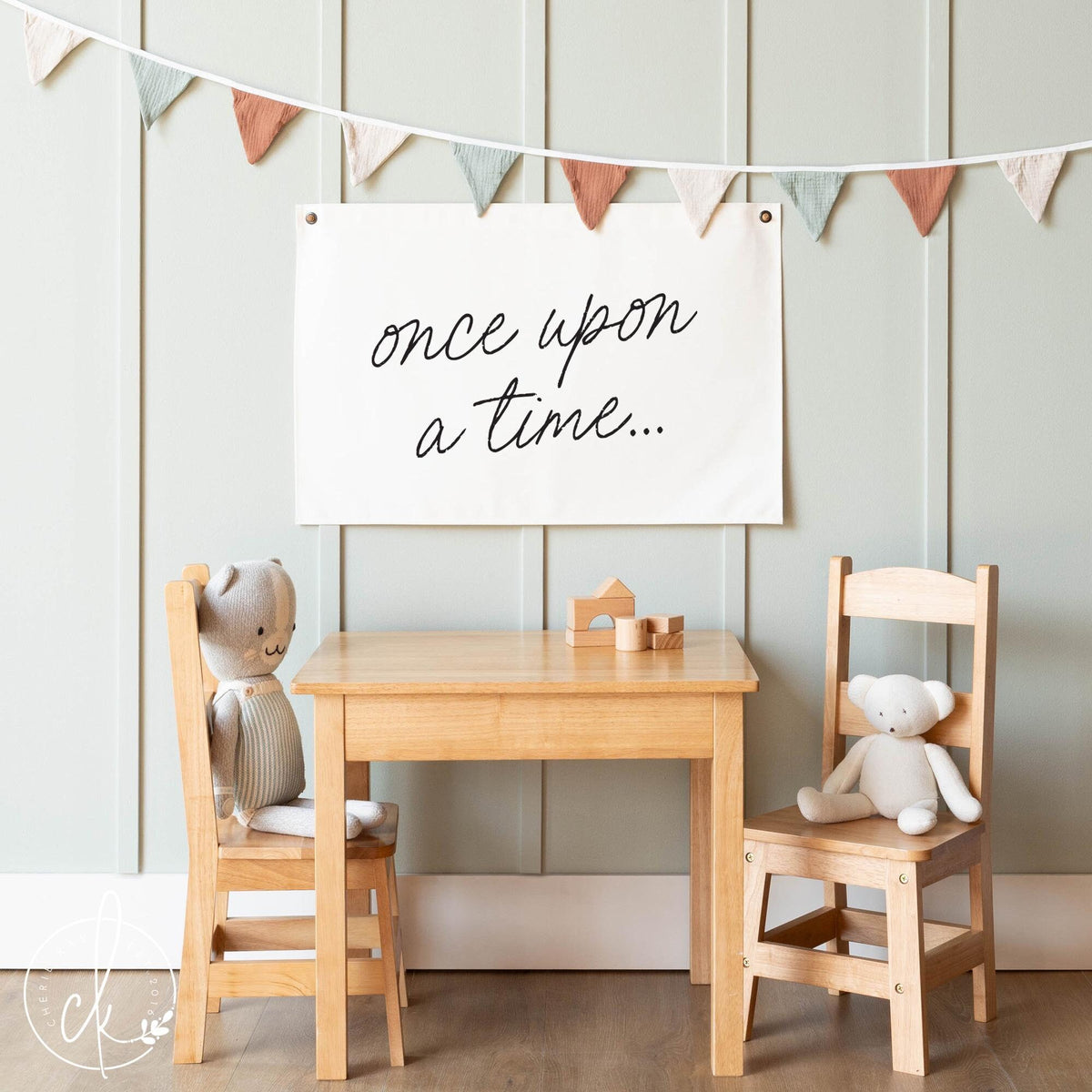 A children&amp;#39;s room with a wooden table, chairs, stuffed animals, and a banner that reads &amp;quot;once upon a time...&amp;quot; hanging on the wall.