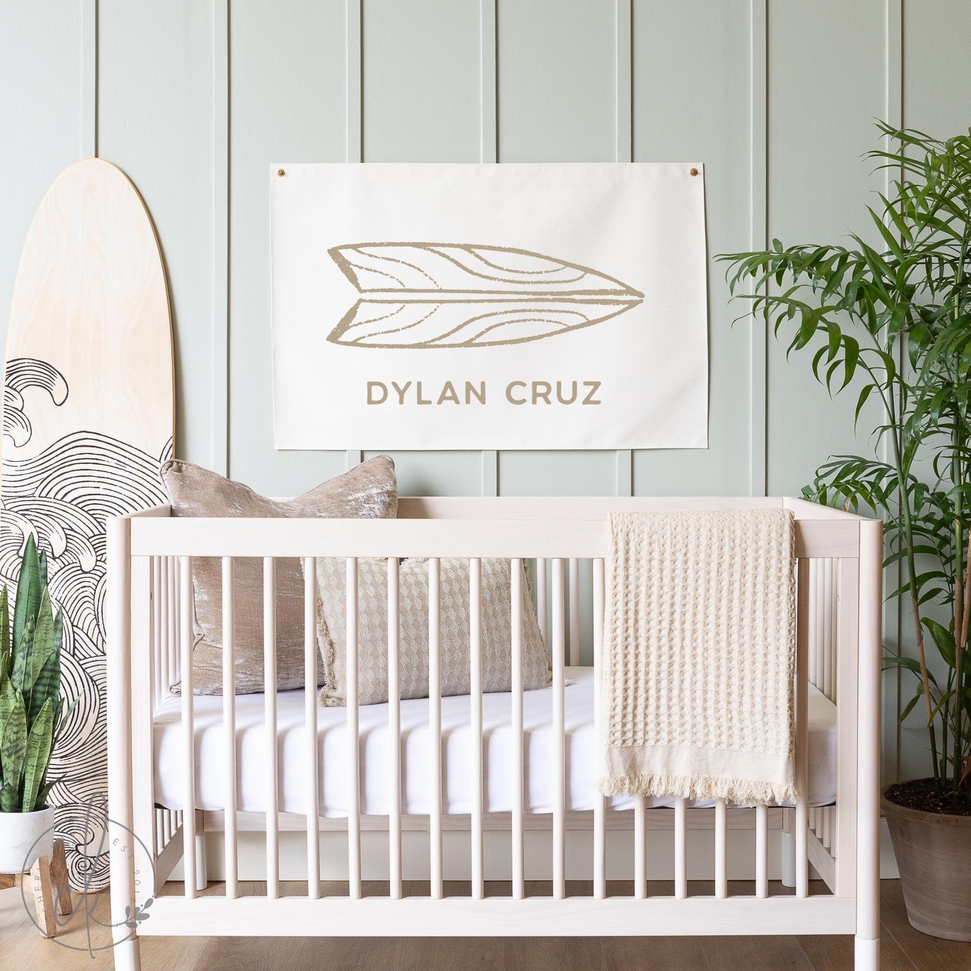 Modern nursery with a beach-themed decor featuring a personalized surfboard name sign that reads Dylan Cruz above a light wooden crib, accompanied by a surfboard graphic and a plant, creating a serene and stylish coastal atmosphere.