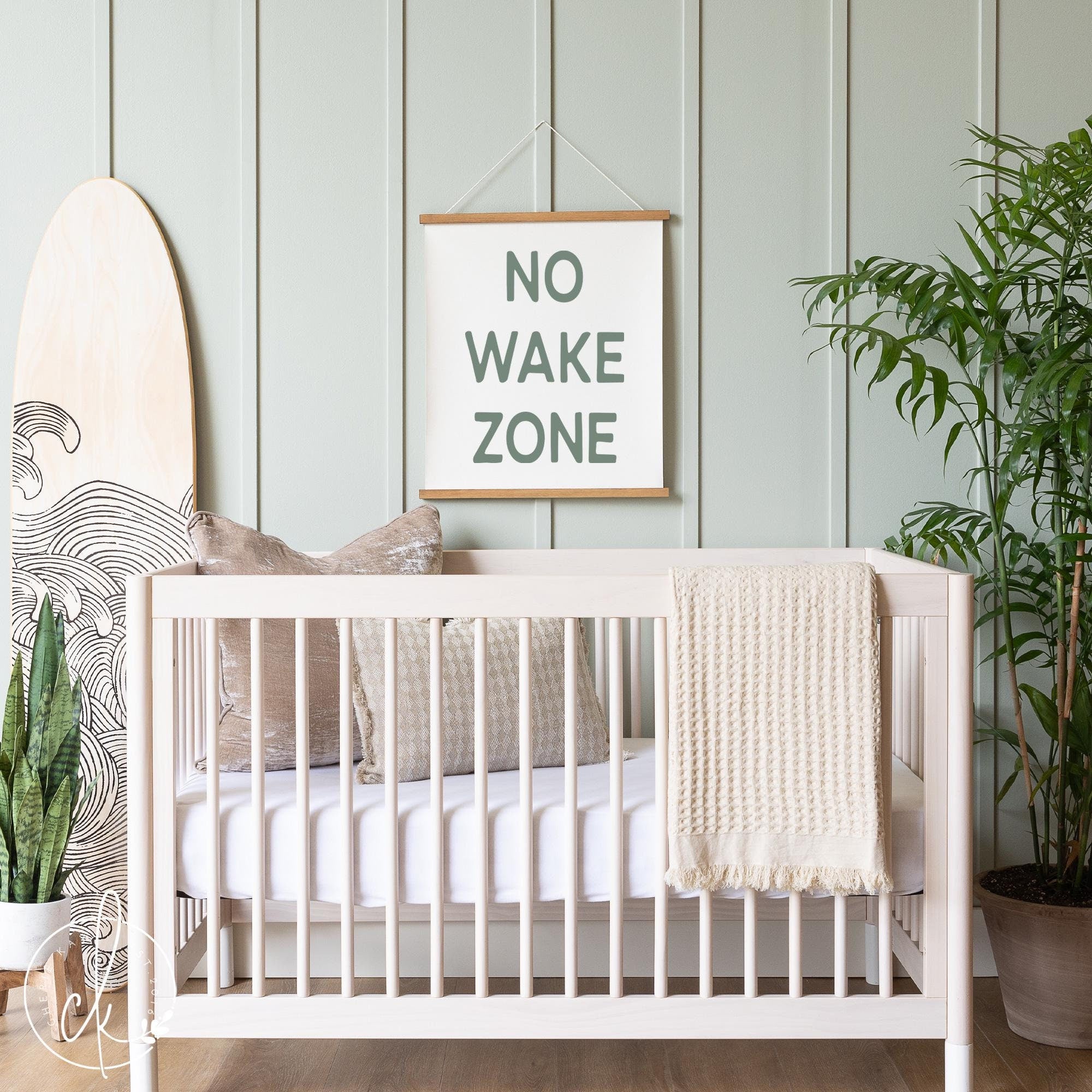 Coastal-themed nursery with NO WAKE ZONE canvas sign, surfboard decor, and natural wood crib, creating a serene beach-inspired baby room.