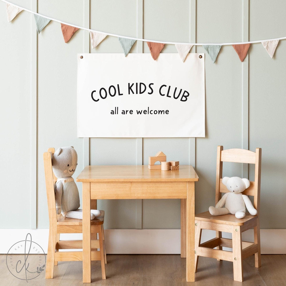 Cool Kids Club All Are Welcome canvas banner hanging in a cozy kids&amp;#39; playroom with wooden furniture and soft toys, perfect for neutral nursery decor, playroom wall art, or classroom decoration.