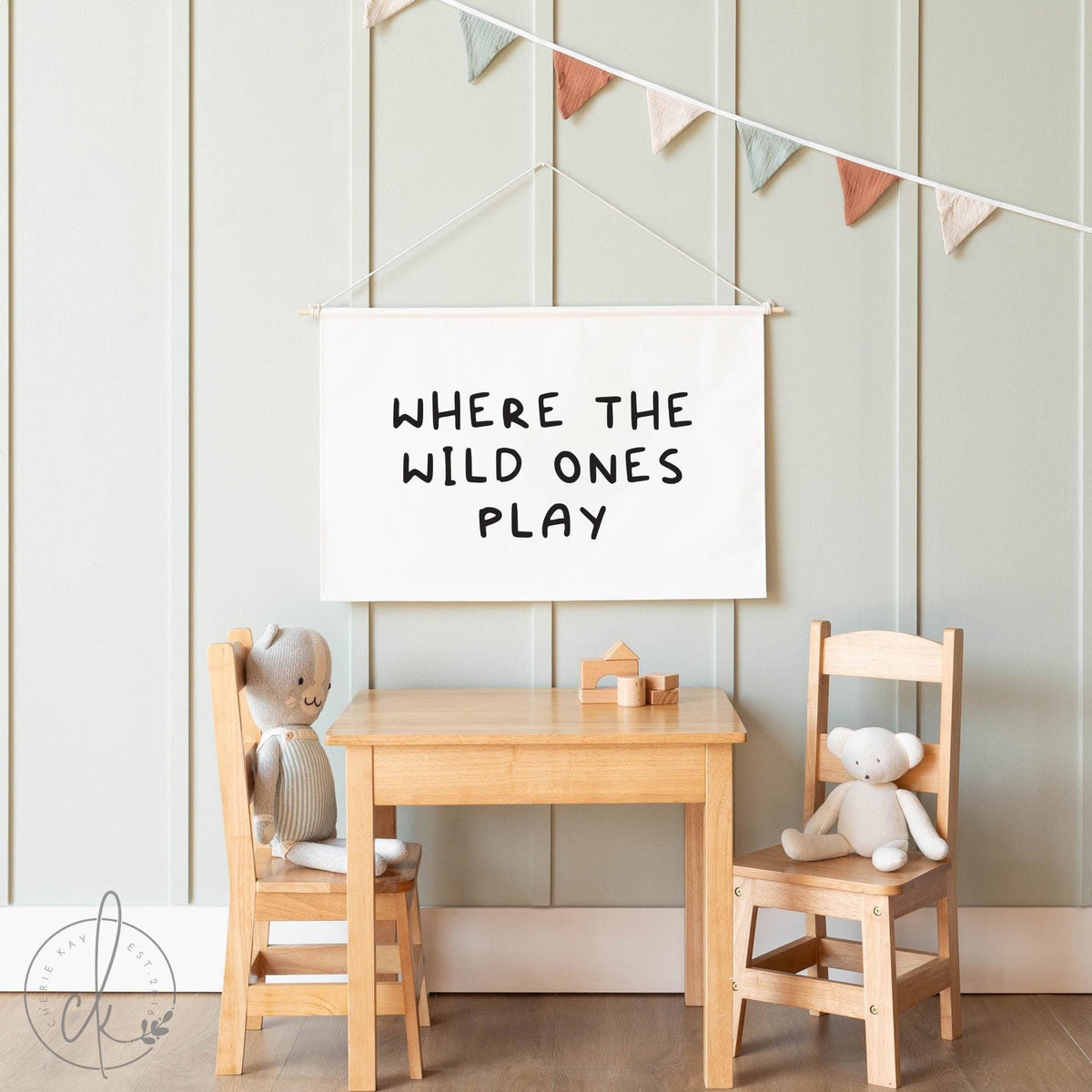 A kids playroom with a wooden table, chairs, soft toys, and a banner reading Where the Wild Ones Play in a cozy, minimalist style.