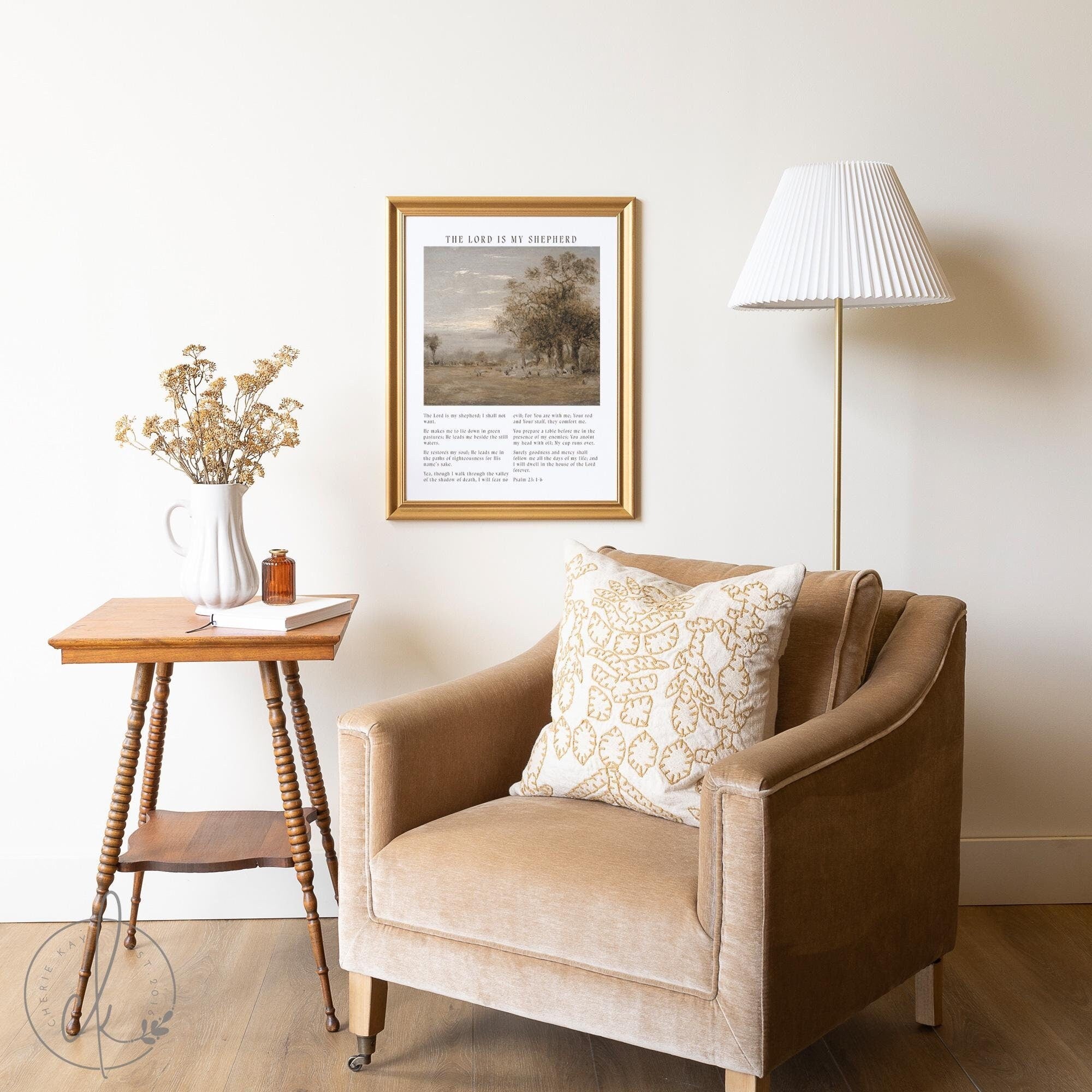 Framed vintage Psalm 23 wall art in a gold frame above a cozy armchair, side table, and dried flower arrangement in a rustic living room setting.