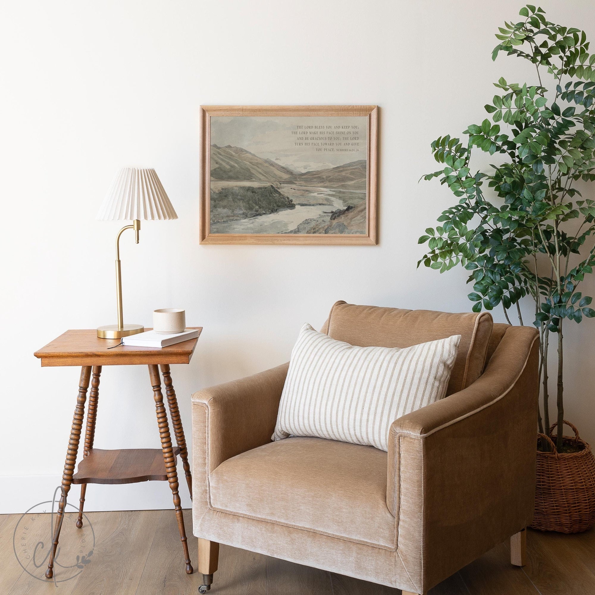 Cozy living room with vintage framed landscape art, beige armchair, wooden side table, and a potted plant.