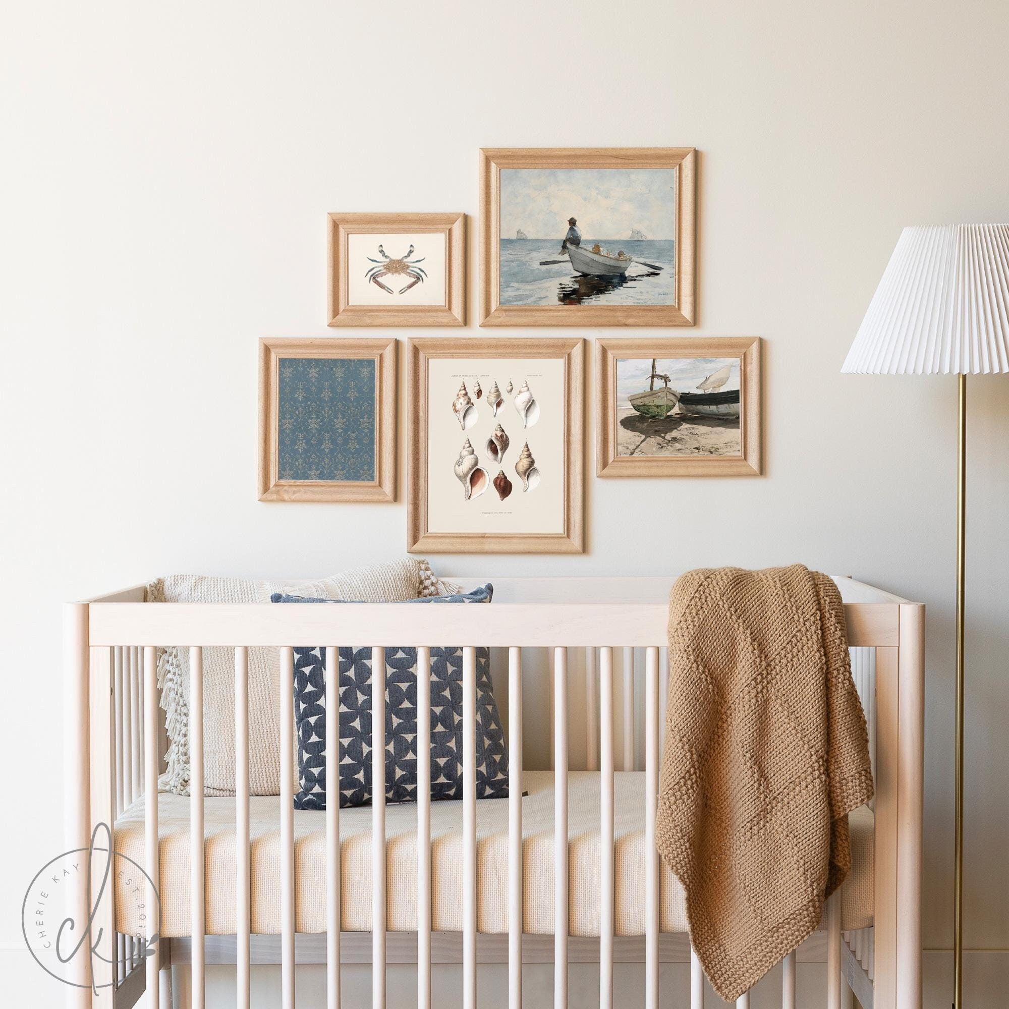 Vintage coastal art collage featuring framed ocean-themed prints with seashells, boats, and crabs, styled as wall decor above a neutral-colored crib in a beach-themed nursery. Perfect for coastal or beach house decor.