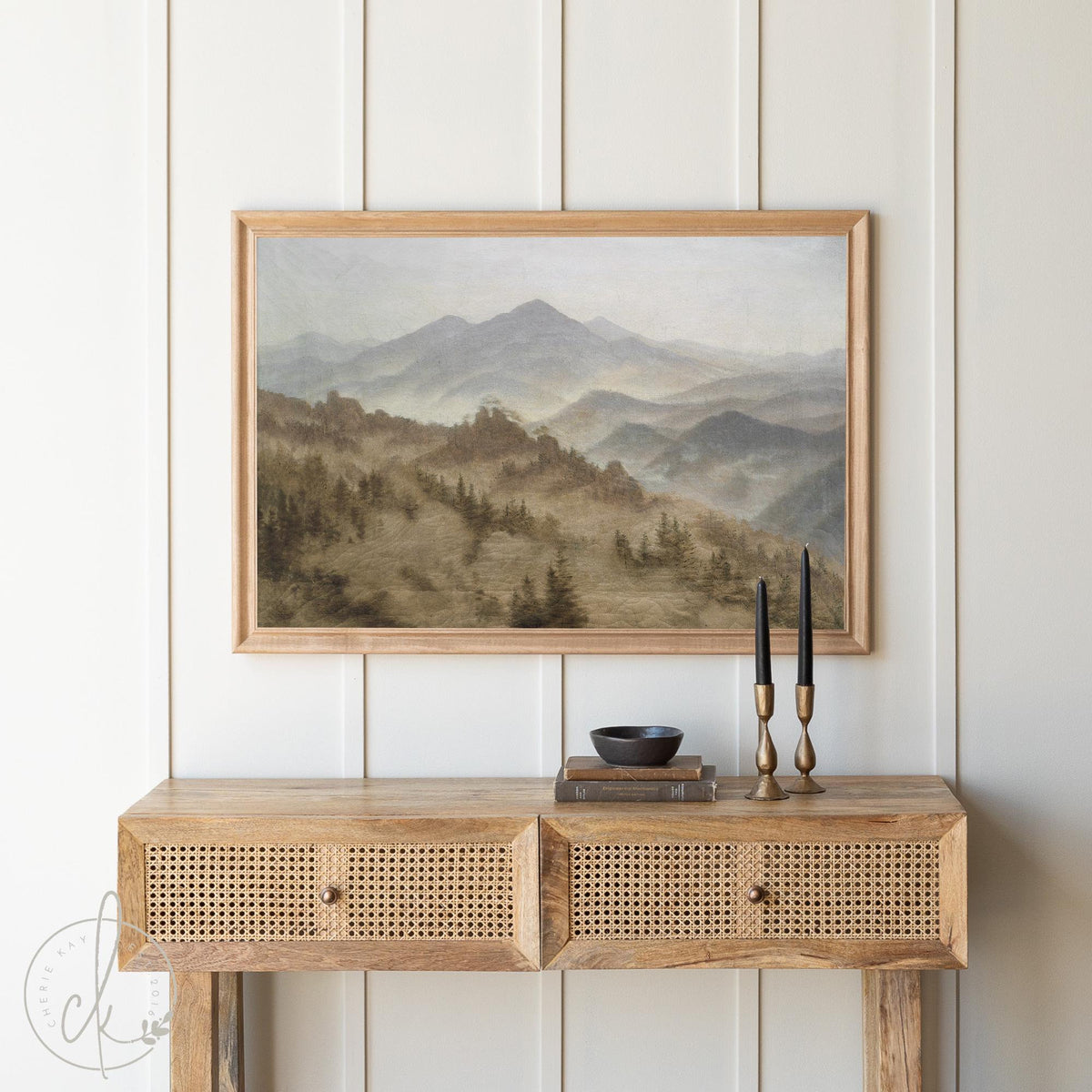 Framed mountain landscape art print with misty forest scene in a gold frame, displayed above a rustic wooden console table. Vintage-inspired wall art featuring serene mountain range, perfect for home decor in living rooms, bedrooms, or office spaces.