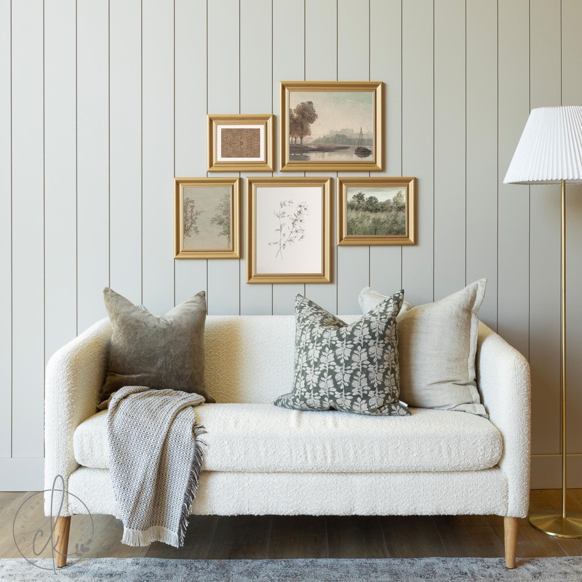 Cozy living room with a gold-framed gallery wall art set featuring minimalist botanical and landscape prints, arranged above a cream-colored textured sofa with decorative pillows and a throw blanket, creating a warm and elegant ambiance.