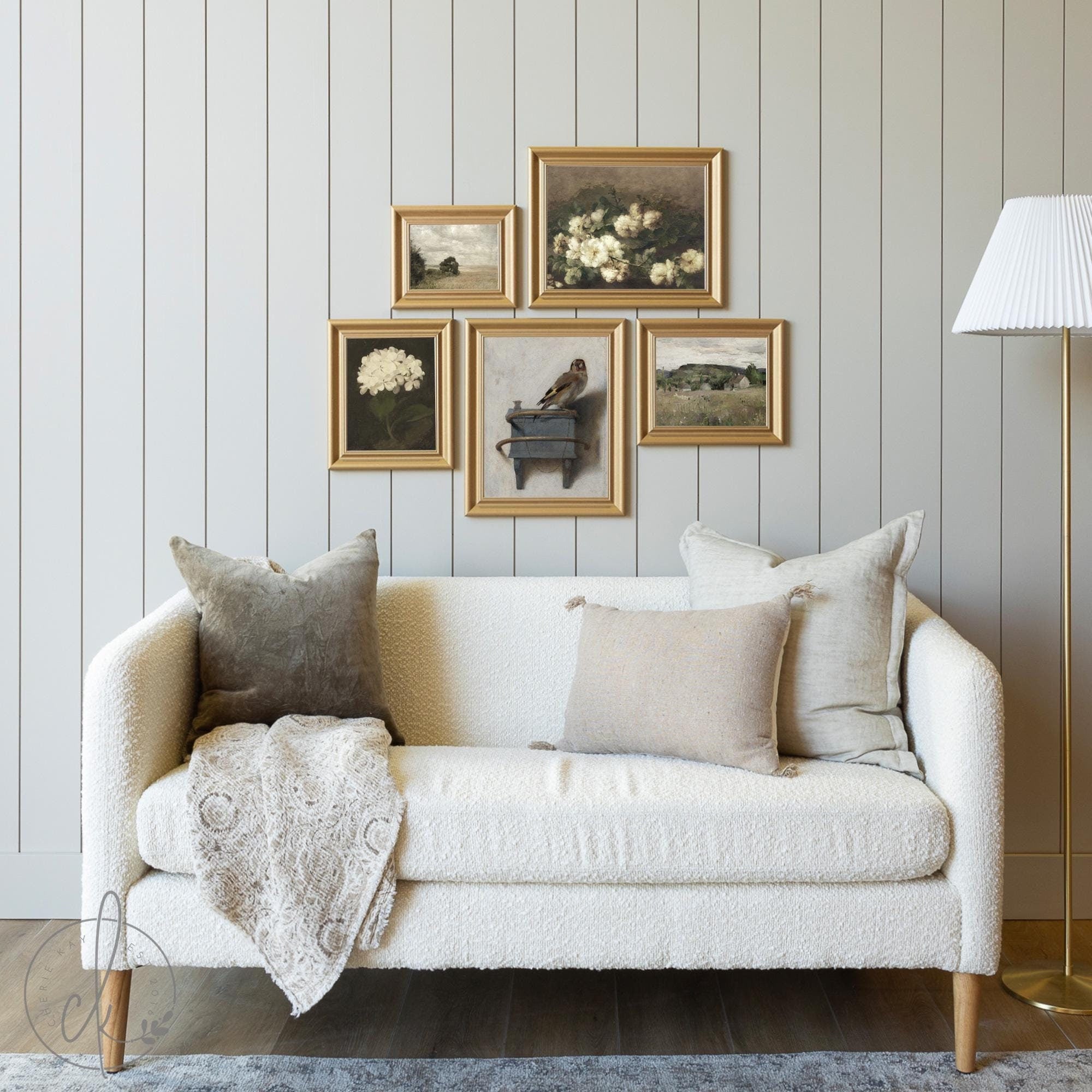 Living room with a white sofa and a gallery wall of vintage-style framed art in gold frames, featuring floral and landscape paintings in a cozy, neutral setting.