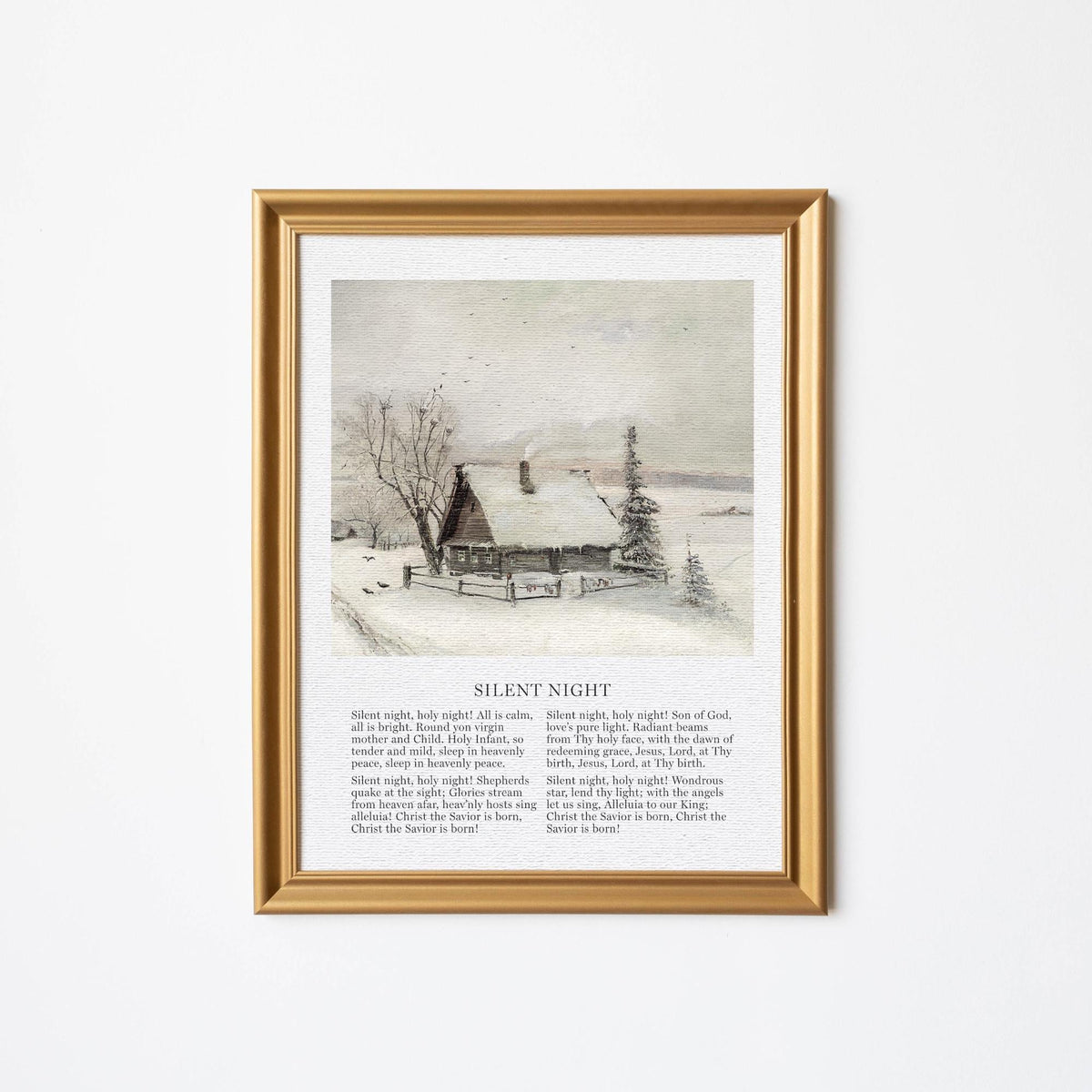 Framed wall art print featuring a peaceful winter scene of a snow-covered cabin and trees, with lyrics to the Christmas carol &amp;quot;Silent Night&amp;quot; below the image. The artwork is displayed in a gold frame on a plain white wall.