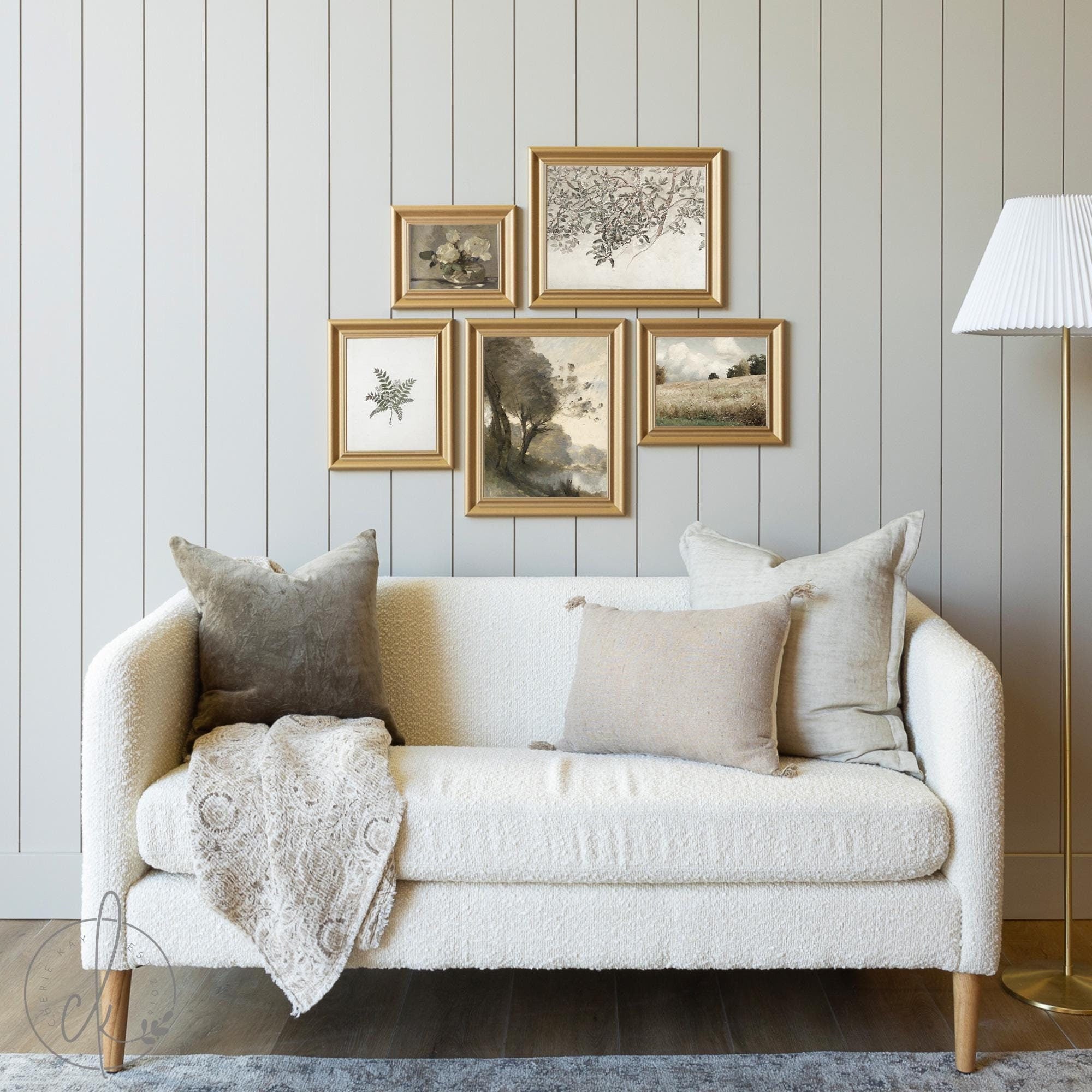 Neutral-toned living room with a cozy white sofa, accented by throw pillows and a knitted blanket. Above, a gallery wall displays vintage-inspired nature prints in gold frames, arranged on a light gray paneled wall for a minimalist, elegant look.