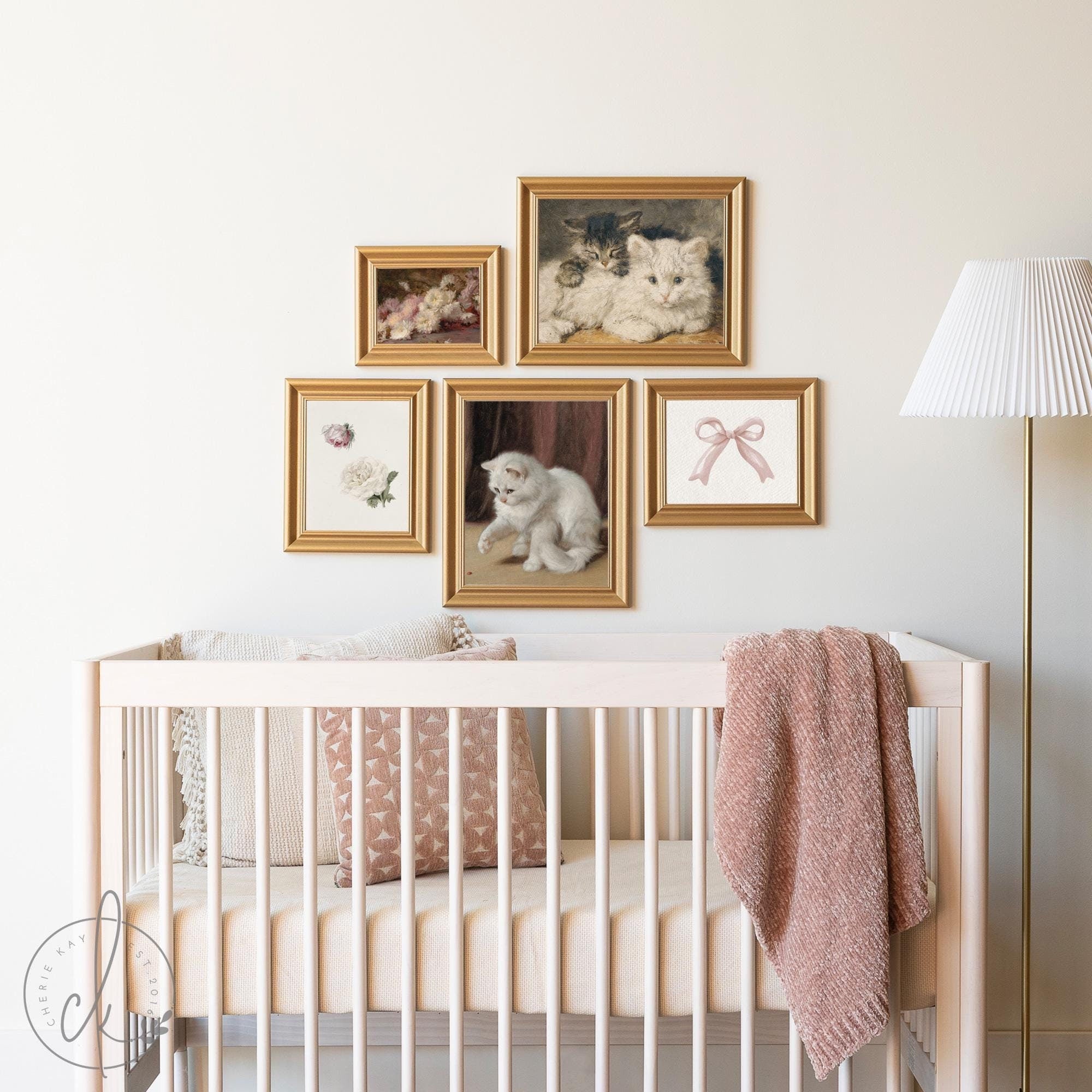 Elegant girl nursery gallery wall art with vintage-inspired framed cat and floral prints, highlighted by pink accents and a soft blanket draped over a crib.