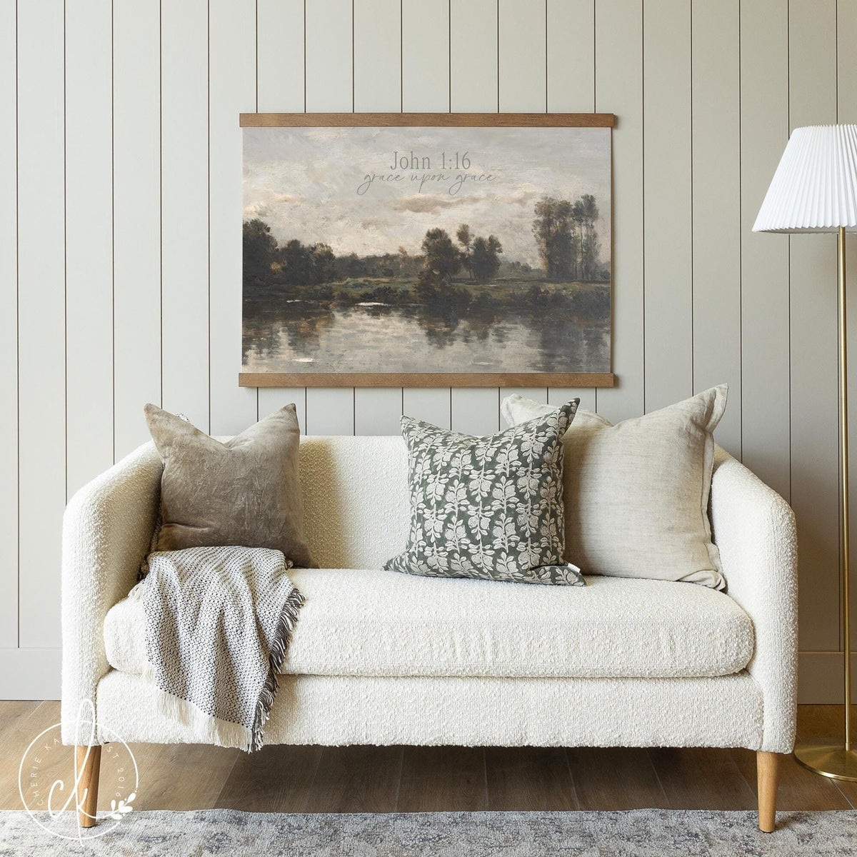 A living room featuring a large landscape wall art with a serene lake scene and the Bible verse John 1:16, &amp;quot;Grace upon grace,&amp;quot; displayed above a white boucle sofa.