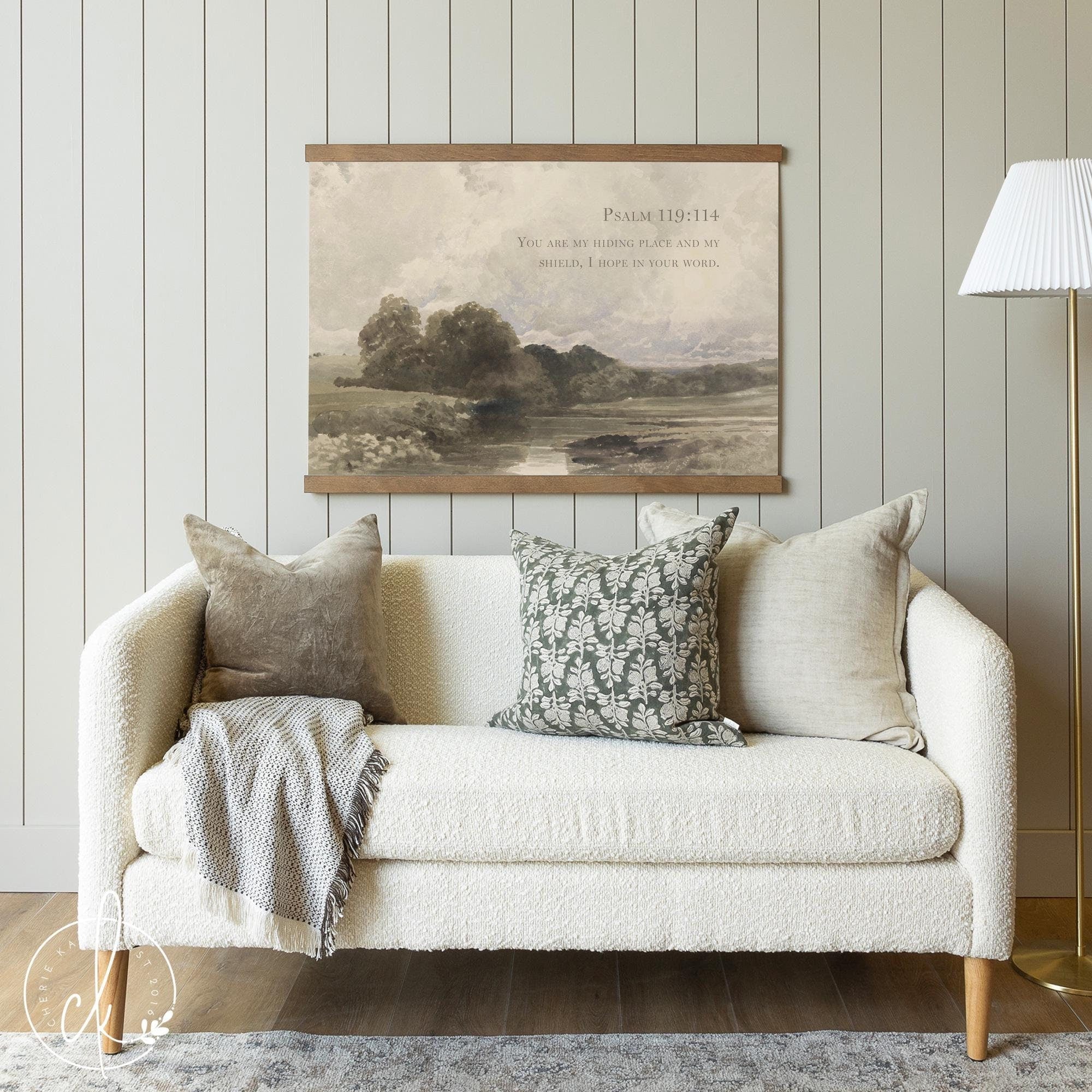 Cozy living room with a neutral-toned sofa, accent pillows, and a vintage-inspired tapestry wall art featuring Psalm 119:114 scripture and a serene countryside landscape, adding a rustic and faith-filled touch to the decor.