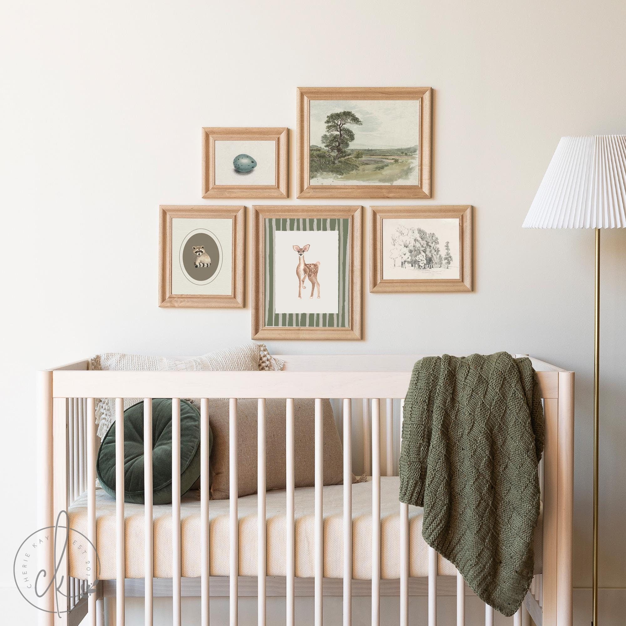 Rustic woodland nursery featuring a crib with neutral bedding, a green knitted blanket, and a gallery wall of framed art prints, including a fawn, raccoon, bird egg, and nature landscapes, in natural wood frames.