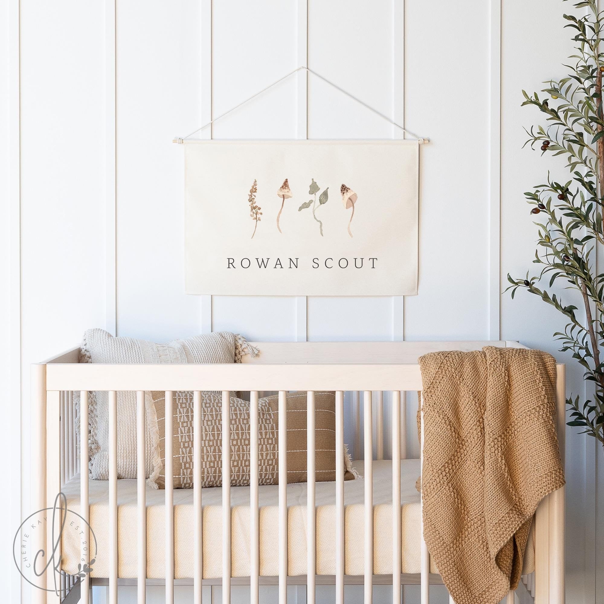 Neutral-toned nursery with a personalized baby name sign featuring botanical illustrations hanging above a wooden crib, styled with cozy pillows, a textured blanket, and natural decor elements.