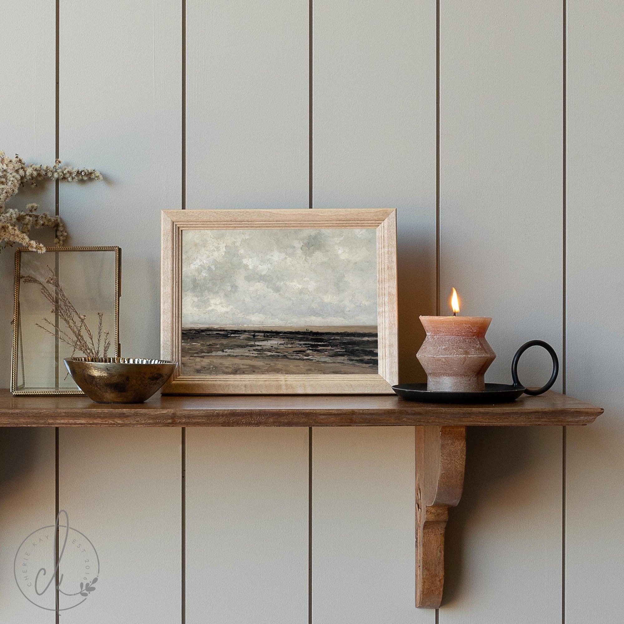 Small framed neutral coastal landscape art print on a shelf, featuring a calming seascape and rustic wood frame for modern farmhouse decor.