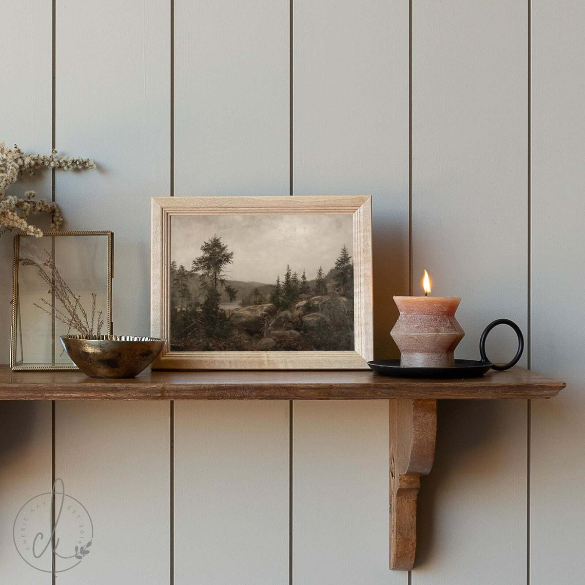 Framed mountain landscape art print with a wooden frame, featuring a serene nature scene on a cozy wooden shelf with a candle and decorative accents.