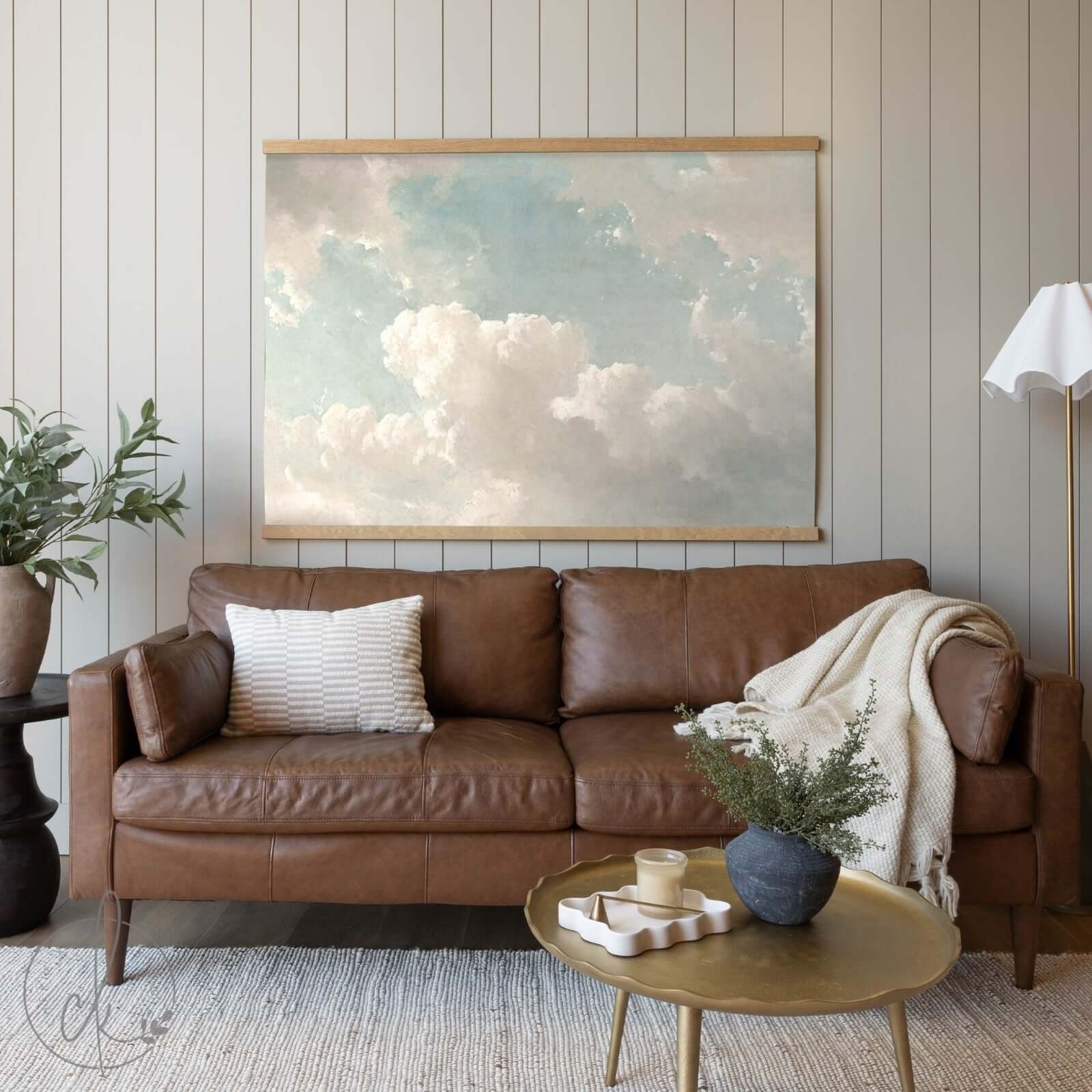 A cozy living room with a brown leather sofa, a gold-toned coffee table, and a large cloud painting on the wall.