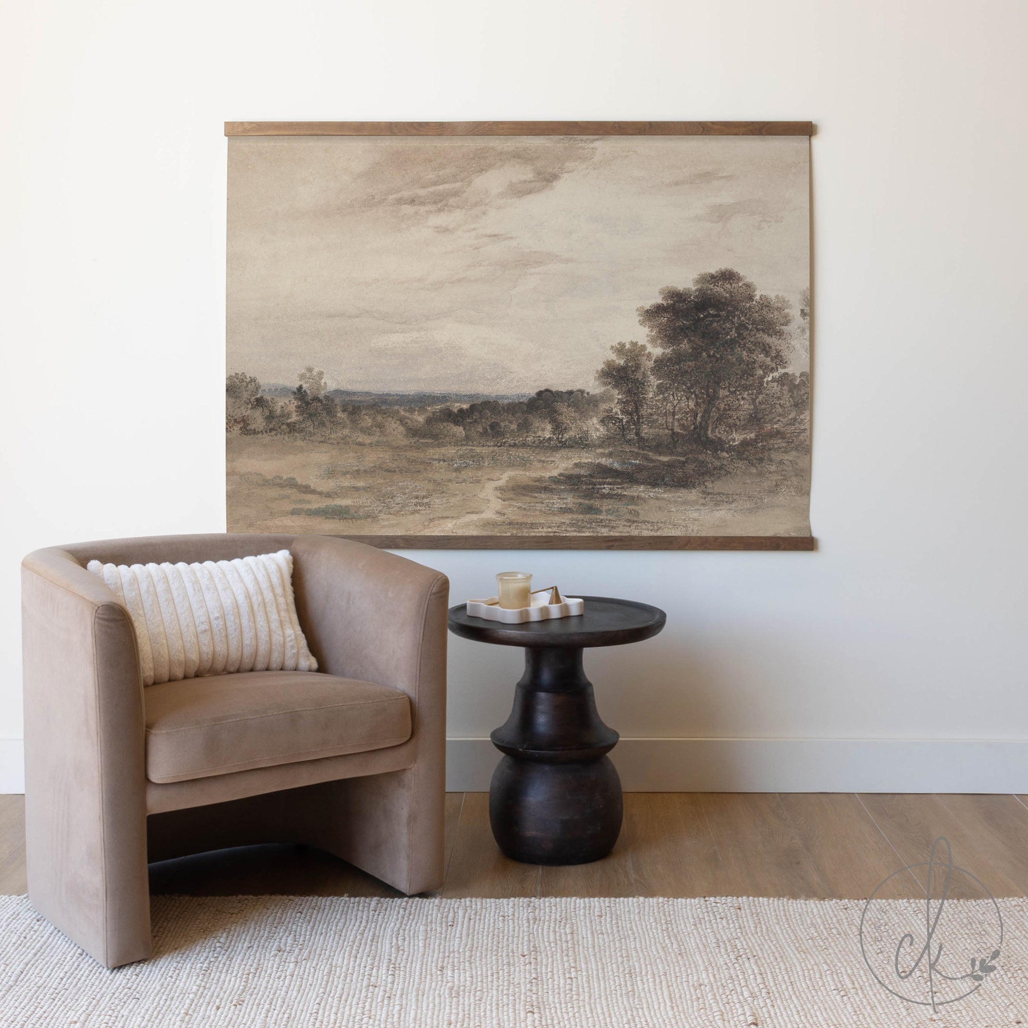 A beige armchair next to a black side table with a candle, with a large painting of a landscape on the wall behind.